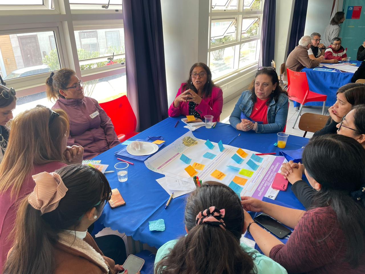 Mujeres sentadas alrededor de una mesa realizando trabajo participativo en papelógrafo
