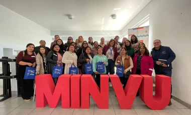 Grupo de personas de pie detrás de letras grandes que conforman la sigla MINVU